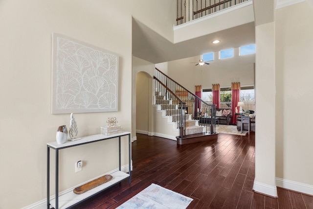 foyer with ceiling fan, a towering ceiling, and wood-type flooring