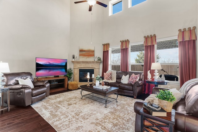 living area with a glass covered fireplace, dark wood finished floors, a towering ceiling, and ceiling fan