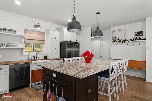 kitchen with white cabinets, black fridge, light hardwood / wood-style flooring, stainless steel dishwasher, and a kitchen island