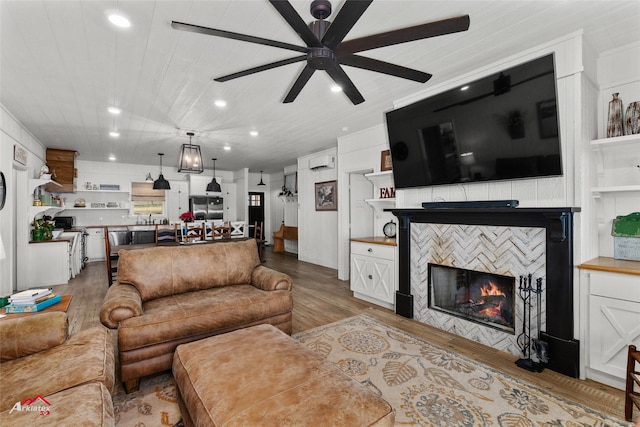 living room with a tile fireplace, built in shelves, light wood-type flooring, and ceiling fan