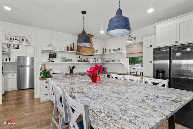 kitchen featuring white cabinets, stainless steel fridge, hardwood / wood-style floors, and pendant lighting