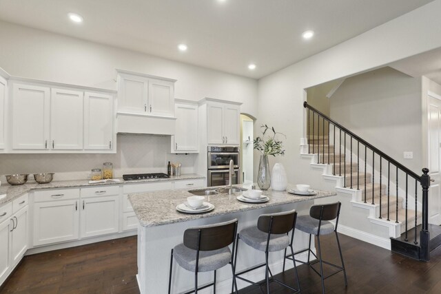 kitchen with white cabinetry, a center island with sink, and light stone counters