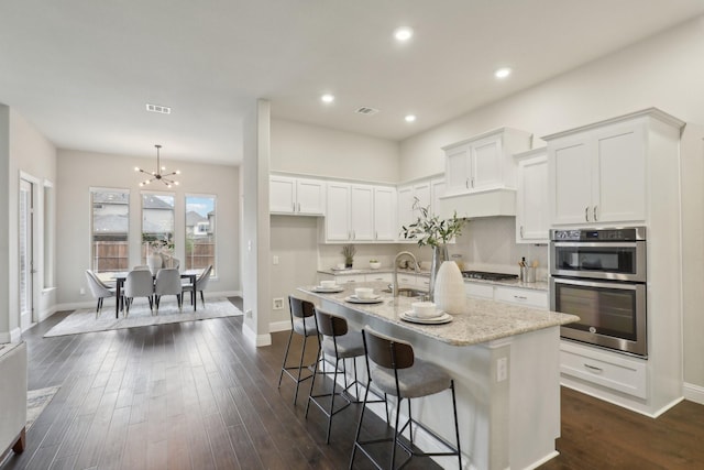 kitchen with white cabinetry, appliances with stainless steel finishes, dark wood-type flooring, and an island with sink