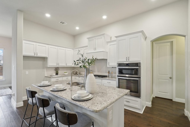 kitchen featuring white cabinetry, a kitchen island with sink, sink, and light stone counters