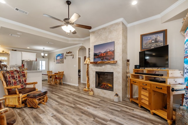 living room with a tiled fireplace, ceiling fan, light wood-type flooring, and ornamental molding