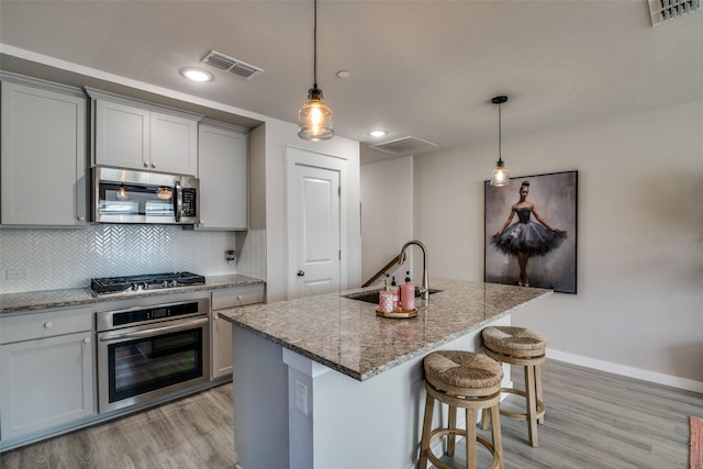 kitchen with appliances with stainless steel finishes, sink, a kitchen island with sink, and gray cabinetry