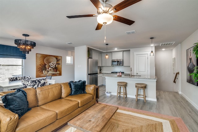 living room featuring ceiling fan with notable chandelier, sink, and light hardwood / wood-style flooring