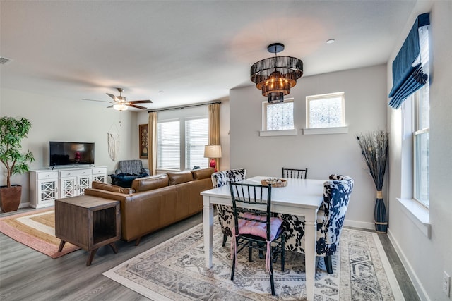 dining space featuring ceiling fan with notable chandelier and wood-type flooring