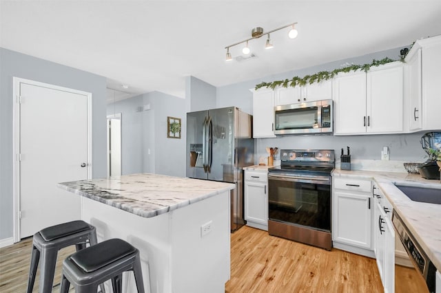 kitchen with appliances with stainless steel finishes, light hardwood / wood-style flooring, white cabinetry, and a kitchen island