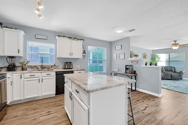 kitchen featuring light stone countertops, a kitchen island, sink, dishwasher, and white cabinetry