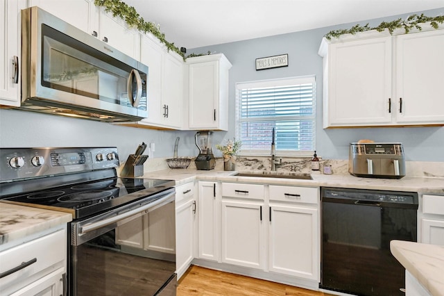 kitchen with light stone countertops, sink, black appliances, light hardwood / wood-style flooring, and white cabinets