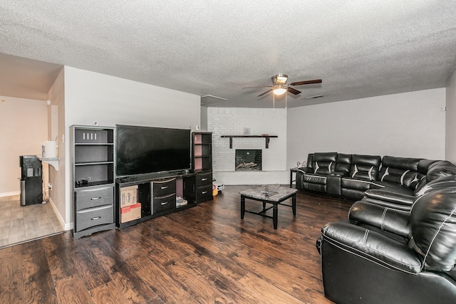 living room with a textured ceiling, ceiling fan, dark wood-type flooring, and a brick fireplace