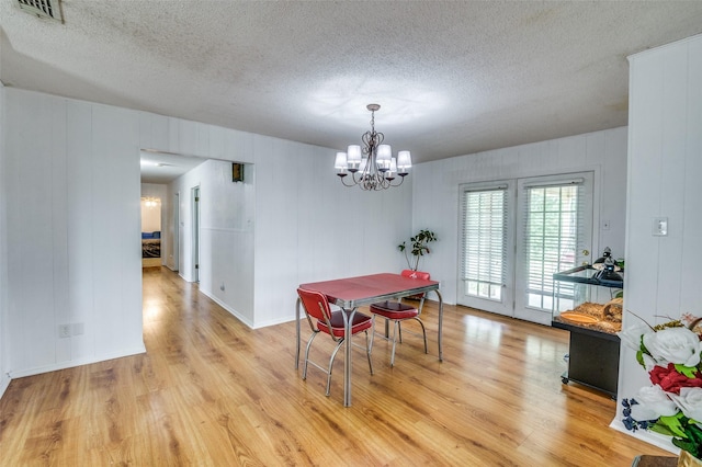 dining area with an inviting chandelier, light hardwood / wood-style floors, and a textured ceiling