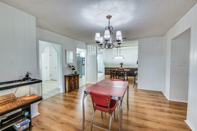 dining room with a chandelier, a textured ceiling, light hardwood / wood-style floors, and wooden walls