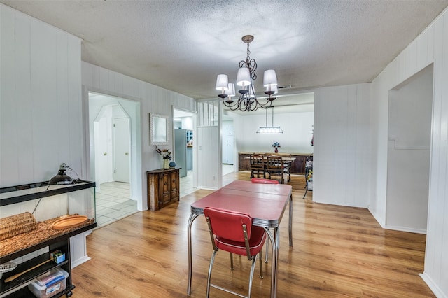 dining area featuring light hardwood / wood-style floors, a textured ceiling, and a notable chandelier