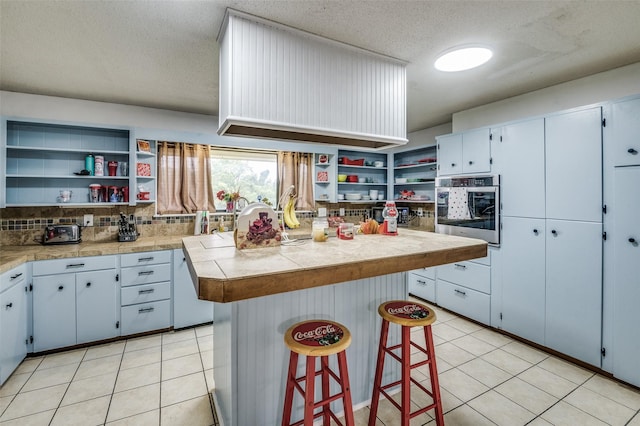 kitchen with backsplash, a kitchen bar, a center island, stainless steel oven, and a textured ceiling