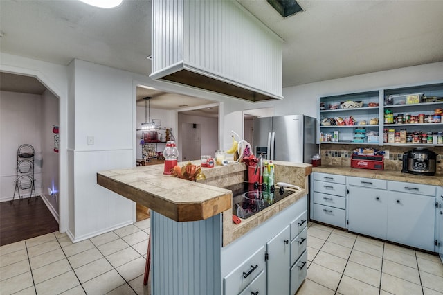 kitchen with stainless steel fridge, hanging light fixtures, tile counters, black electric stovetop, and light tile patterned floors