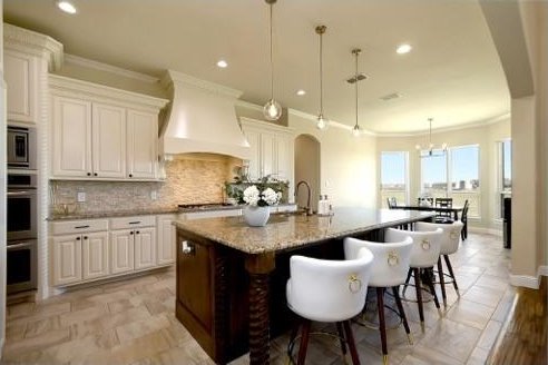 kitchen with light stone counters, premium range hood, pendant lighting, a breakfast bar, and a center island with sink