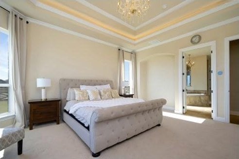 carpeted bedroom with a chandelier, ensuite bathroom, and crown molding