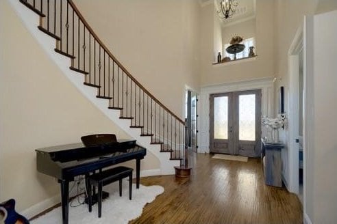 entryway with hardwood / wood-style flooring, a notable chandelier, a towering ceiling, and french doors