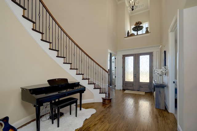 entrance foyer featuring a towering ceiling, hardwood / wood-style floors, a chandelier, ornamental molding, and french doors