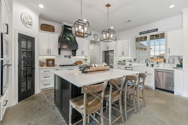 kitchen with stainless steel appliances, white cabinetry, hanging light fixtures, premium range hood, and a kitchen island