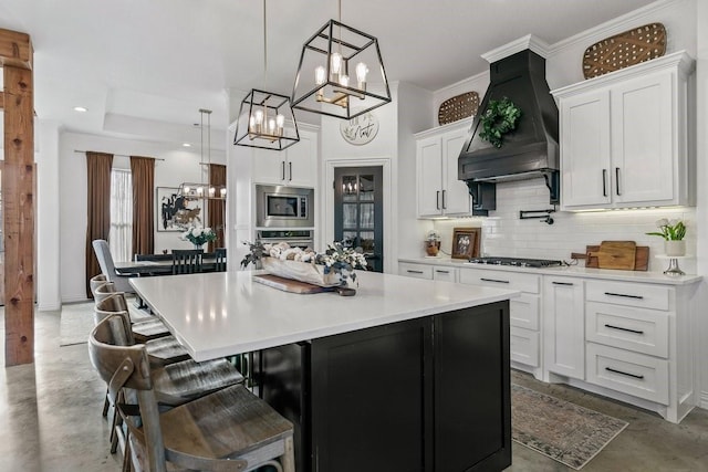 kitchen with decorative light fixtures, white cabinetry, premium range hood, and appliances with stainless steel finishes