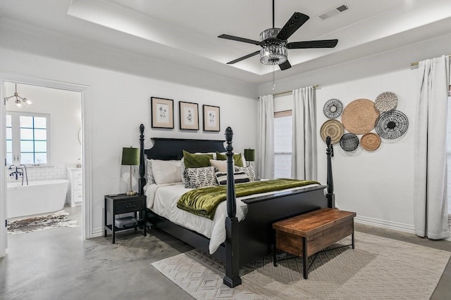 bedroom featuring ensuite bath, concrete floors, a tray ceiling, crown molding, and ceiling fan with notable chandelier