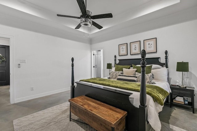 bedroom with ceiling fan, concrete flooring, and a tray ceiling