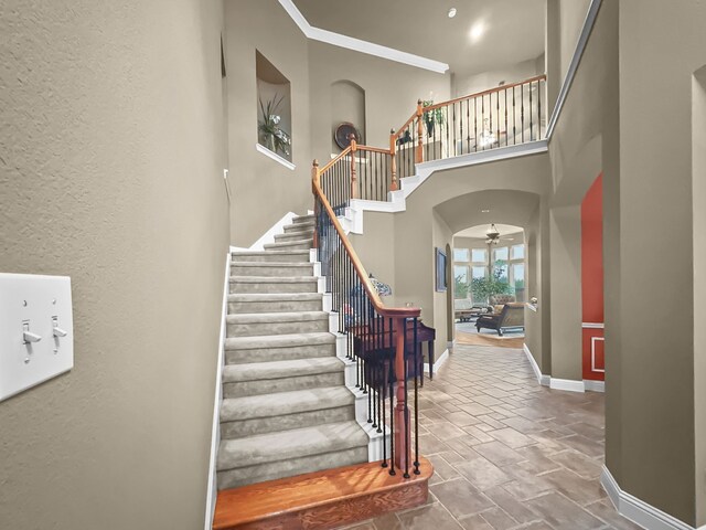 stairs with a towering ceiling, ceiling fan, and ornamental molding