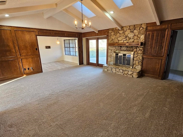 unfurnished living room featuring wood walls, light carpet, a stone fireplace, vaulted ceiling with skylight, and a chandelier