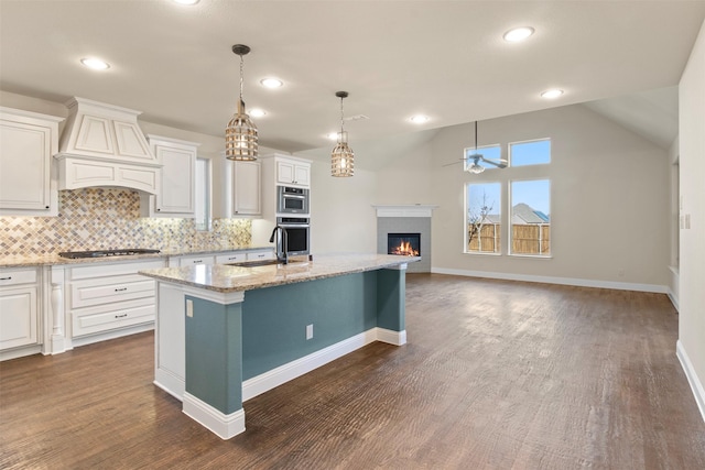 kitchen with light stone counters, dark hardwood / wood-style flooring, premium range hood, a kitchen island with sink, and white cabinets