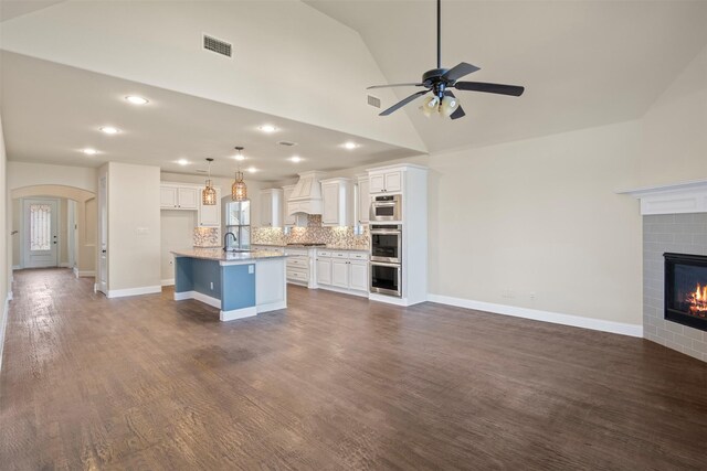 kitchen featuring backsplash, premium range hood, a center island with sink, sink, and hanging light fixtures