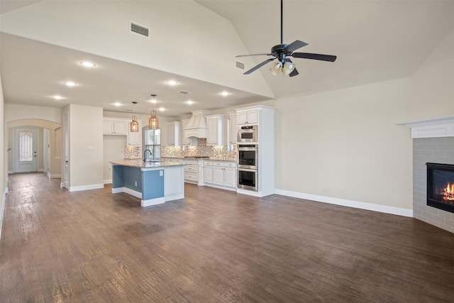 kitchen with white cabinetry, a kitchen island with sink, decorative light fixtures, premium range hood, and sink