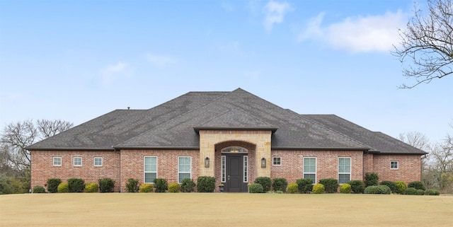 french country inspired facade with a shingled roof, brick siding, and a front lawn