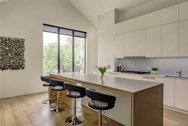 kitchen with a kitchen island, white cabinetry, sink, backsplash, and a breakfast bar