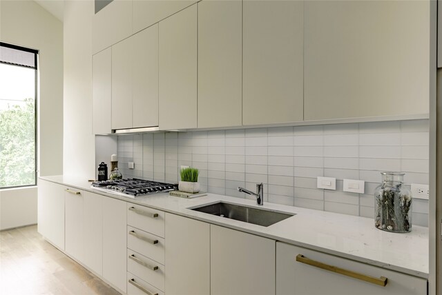 kitchen featuring light stone counters, sink, stainless steel gas cooktop, and tasteful backsplash