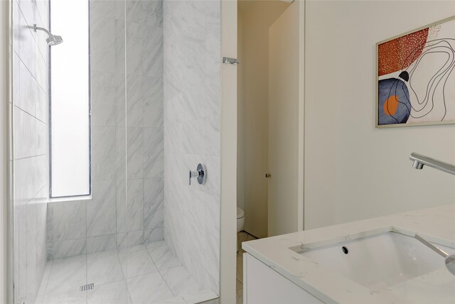 bathroom with toilet, a tile shower, and vanity