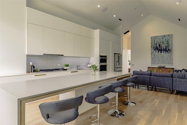 kitchen featuring lofted ceiling, backsplash, light hardwood / wood-style floors, sink, and stainless steel appliances