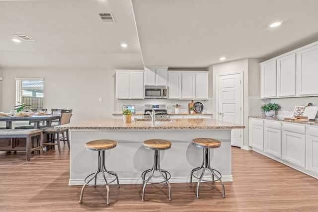 kitchen with white cabinets, light stone counters, stainless steel appliances, and an island with sink