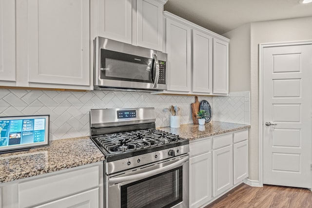 kitchen featuring light stone countertops, appliances with stainless steel finishes, tasteful backsplash, light hardwood / wood-style flooring, and white cabinetry