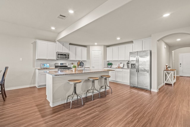 kitchen with decorative backsplash, stainless steel appliances, white cabinetry, and a center island with sink