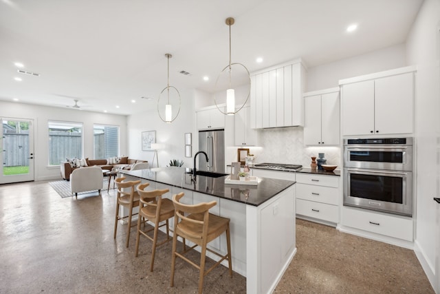 kitchen with decorative light fixtures, a breakfast bar area, a center island with sink, white cabinets, and appliances with stainless steel finishes