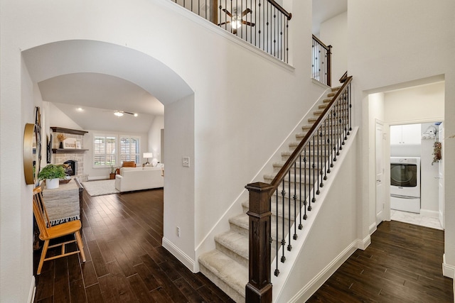 staircase with washer / clothes dryer, hardwood / wood-style flooring, a stone fireplace, and a high ceiling