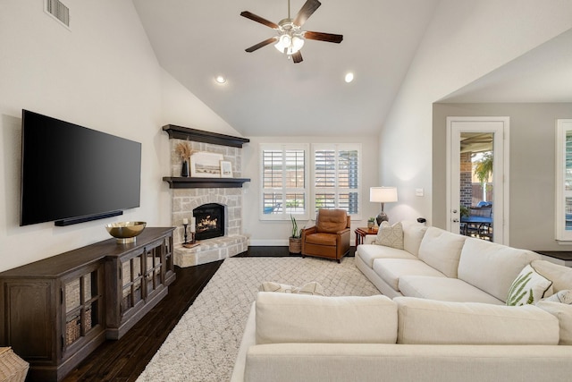 living room featuring ceiling fan, a healthy amount of sunlight, dark hardwood / wood-style floors, and a stone fireplace