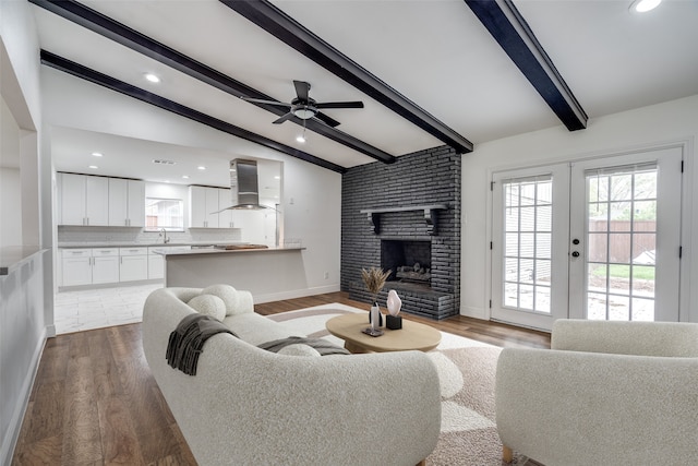 living room with french doors, vaulted ceiling with beams, ceiling fan, a fireplace, and wood-type flooring