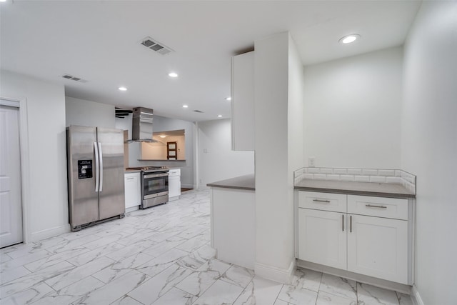 kitchen with appliances with stainless steel finishes, white cabinetry, and wall chimney range hood