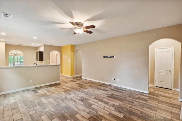 spare room with ceiling fan with notable chandelier and light wood-type flooring