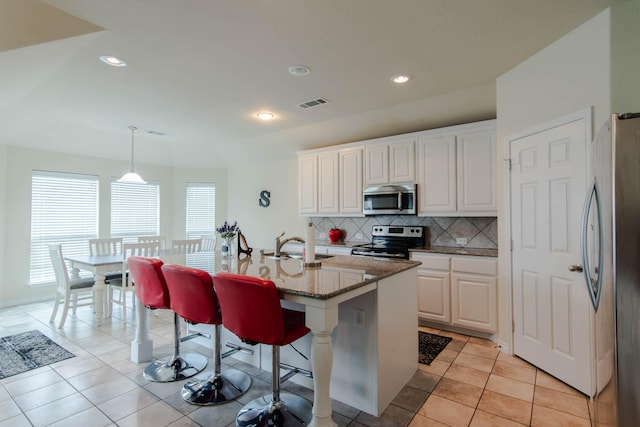 kitchen featuring white cabinetry, hanging light fixtures, a kitchen bar, a kitchen island with sink, and appliances with stainless steel finishes