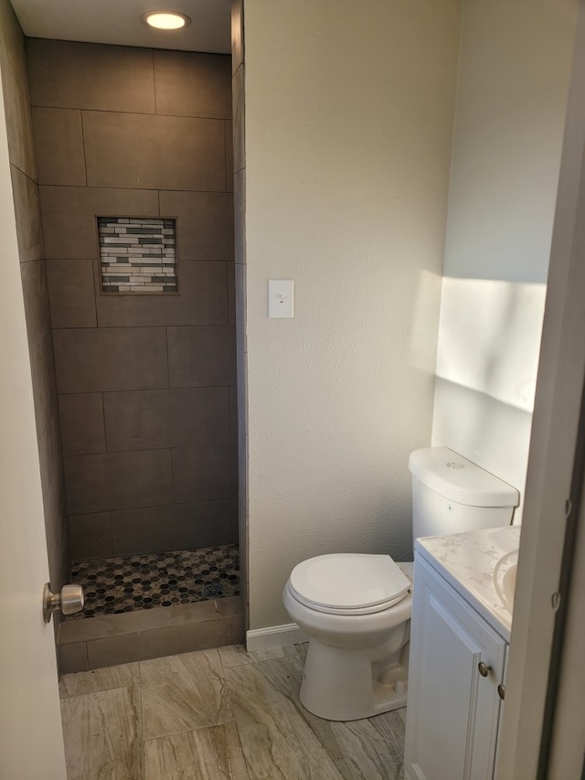 bathroom with vanity, a tile shower, and toilet